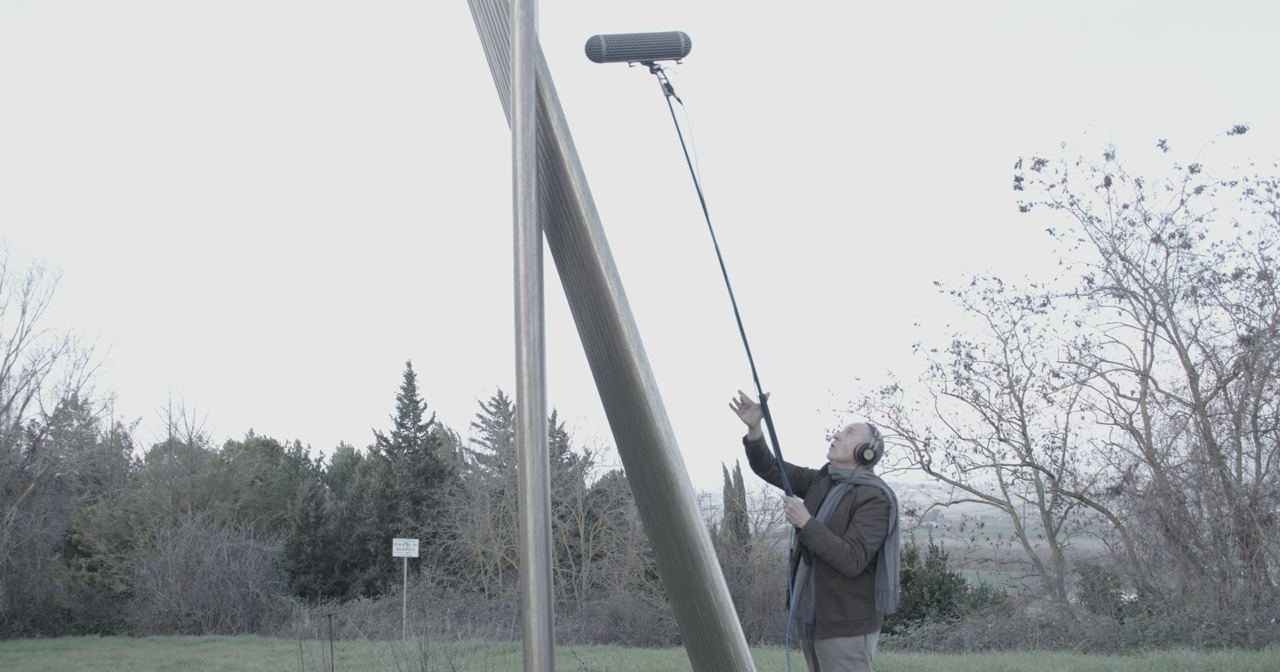 Roberto Rosi con cuffie e microfono su asta registra il suono di una scultura in acciaio all'aperto